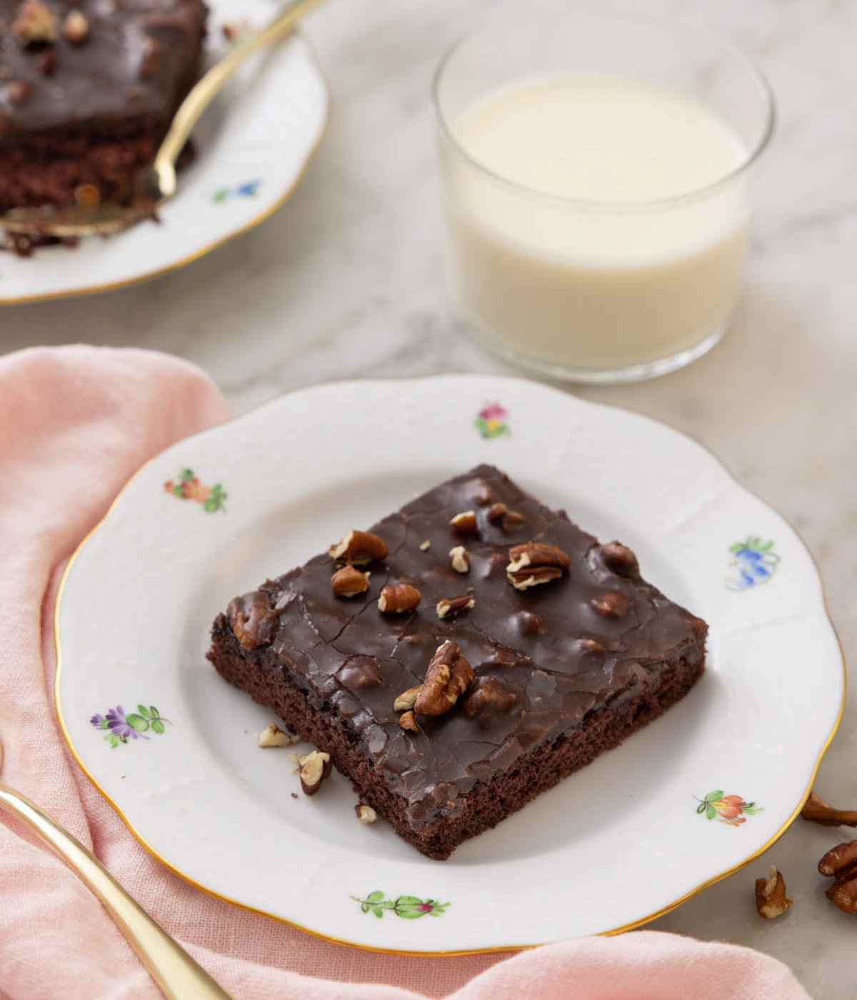 A square slice of Texas sheet cake on a small plate with a glass of milk in the background.