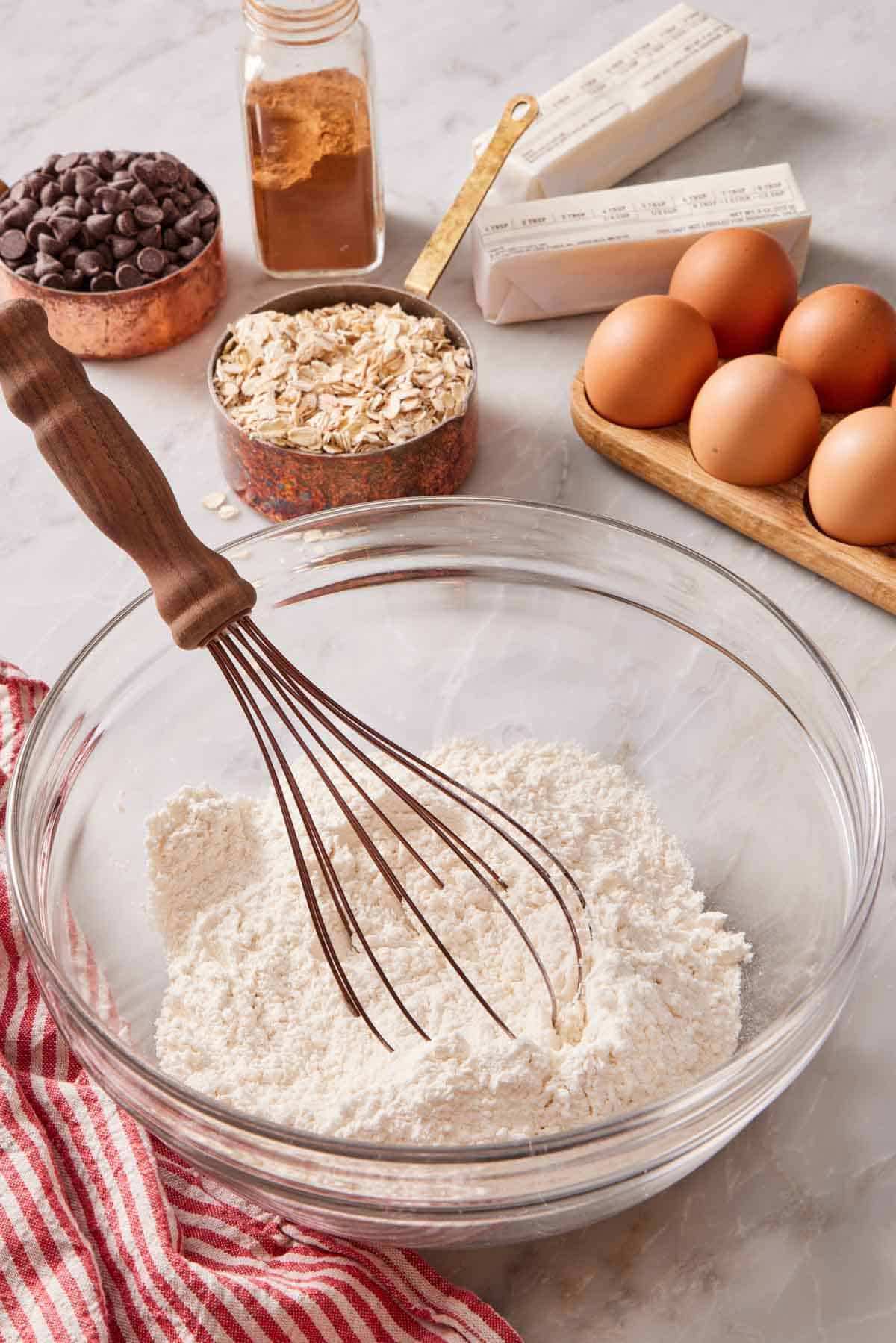 A glass bowl with flour and a whisk, and other baking ingredients behind it.