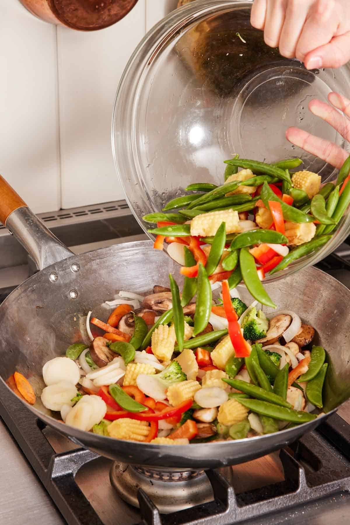 Ingredients for vegetable stir fry poured from a bowl into a wok.