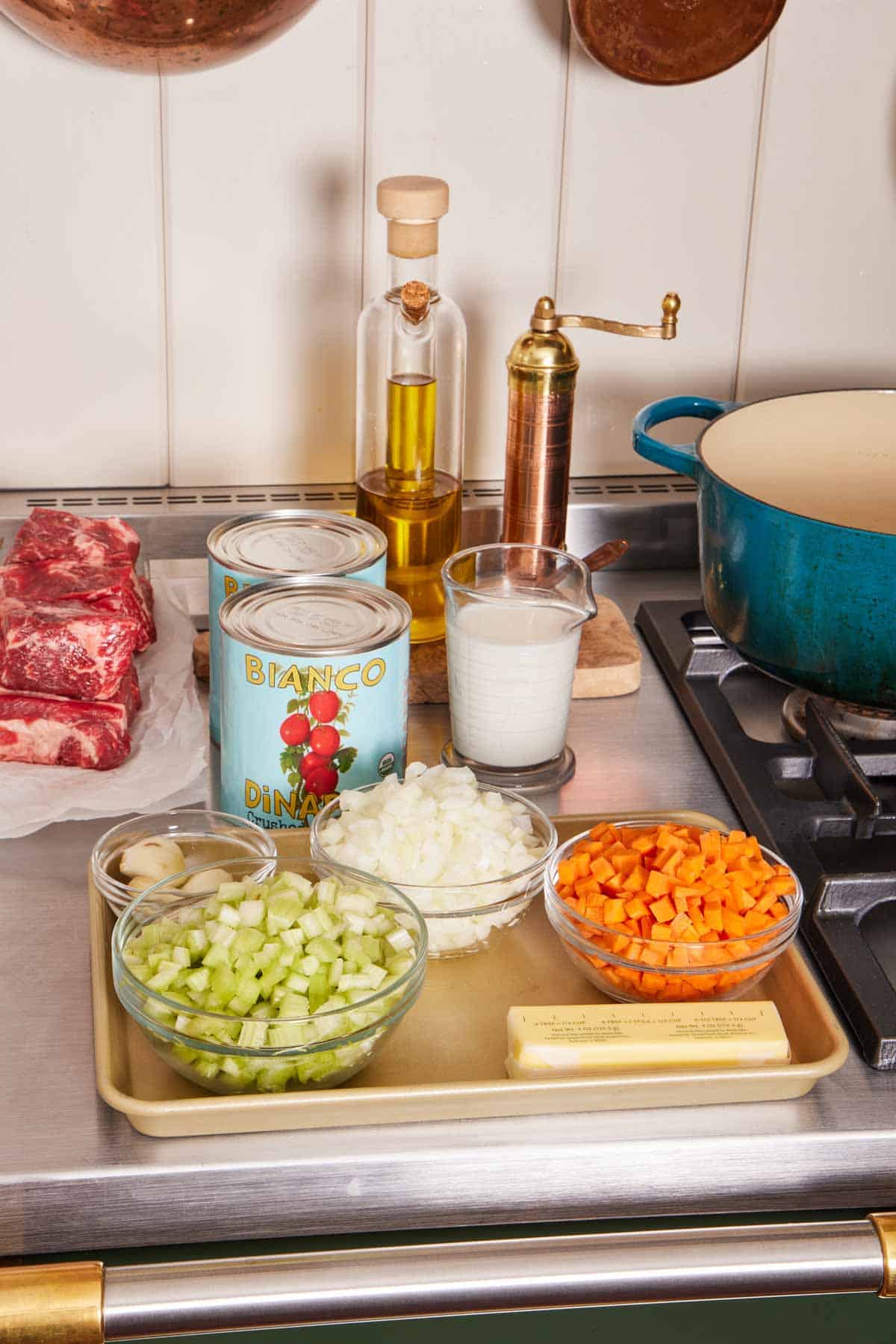 Mise en place with chopped vegetables, canned tomatoes, oil, and beef.