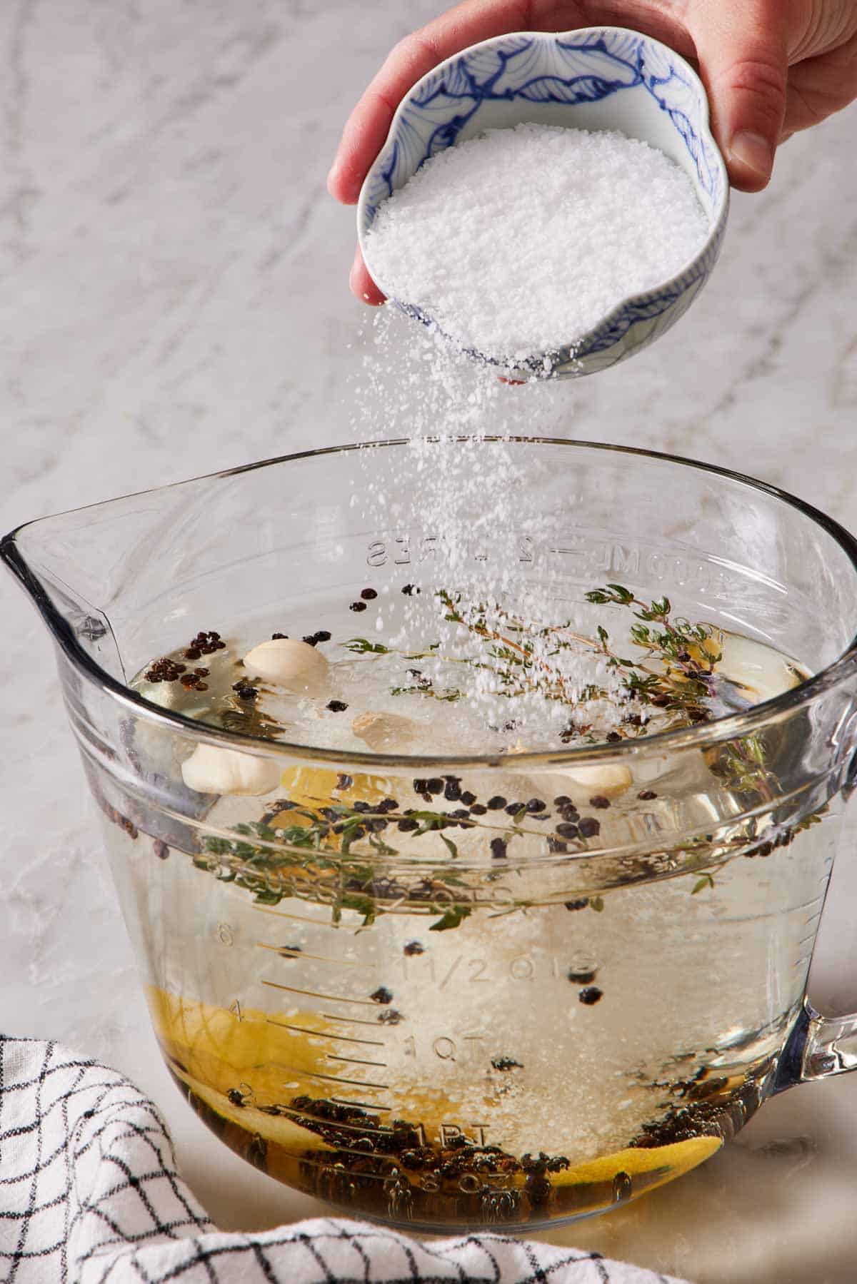 Brine ingredients in a large measuring cup with salt being sprinkled in.