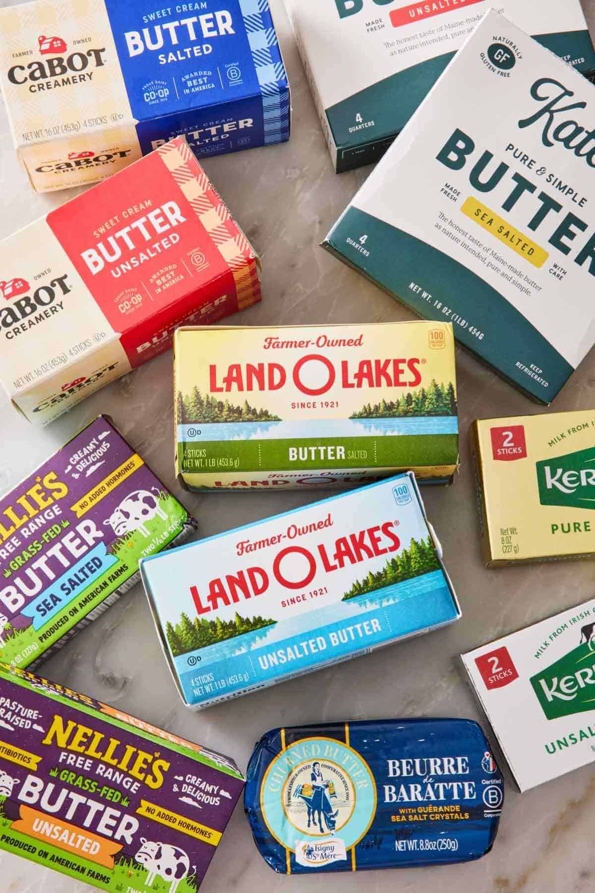 Overhead shot of different brands of butter on a marble countertop.